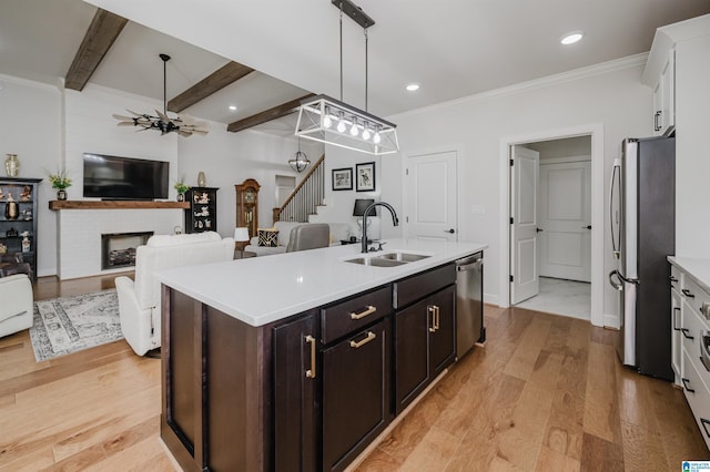 kitchen with a fireplace, a center island with sink, stainless steel appliances, light wood-style floors, and a sink