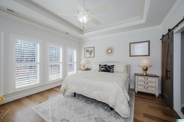 bedroom with wood finished floors, a raised ceiling, visible vents, and a barn door