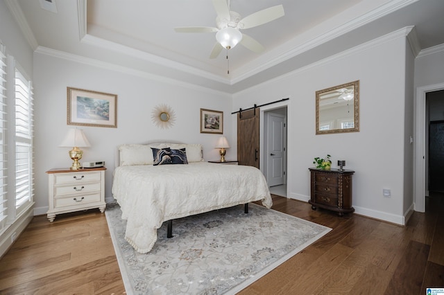 bedroom featuring a raised ceiling, a barn door, wood finished floors, multiple windows, and baseboards