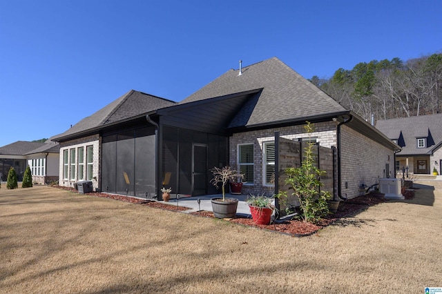 back of house with ac unit, brick siding, a yard, a shingled roof, and a sunroom