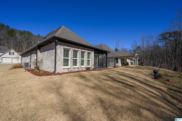 exterior space with roof with shingles, brick siding, a yard, central air condition unit, and a sunroom