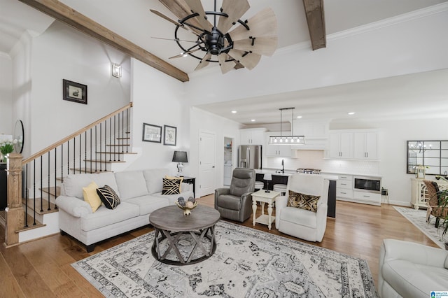 living room with light wood-style floors, stairs, a ceiling fan, and beam ceiling