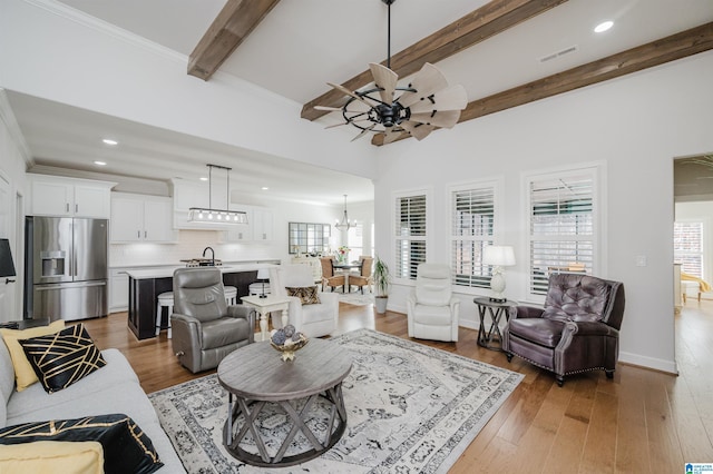 living area featuring ceiling fan with notable chandelier, beamed ceiling, visible vents, and light wood-style floors