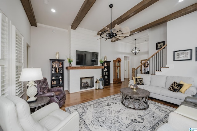 living area with a large fireplace, ceiling fan, stairway, wood finished floors, and beamed ceiling