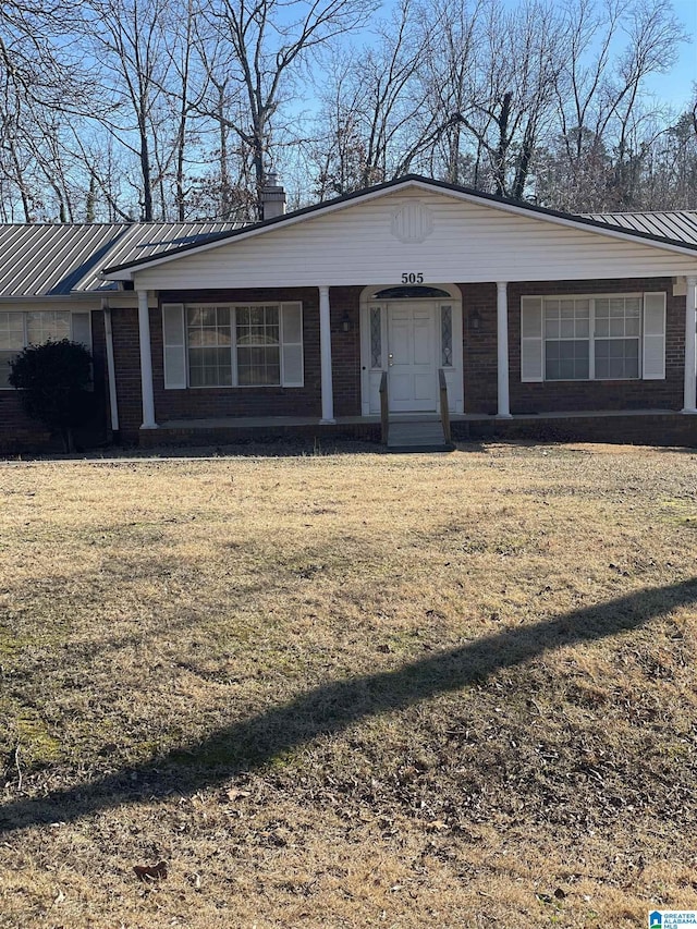 view of front of property with metal roof, brick siding, a chimney, and a front yard