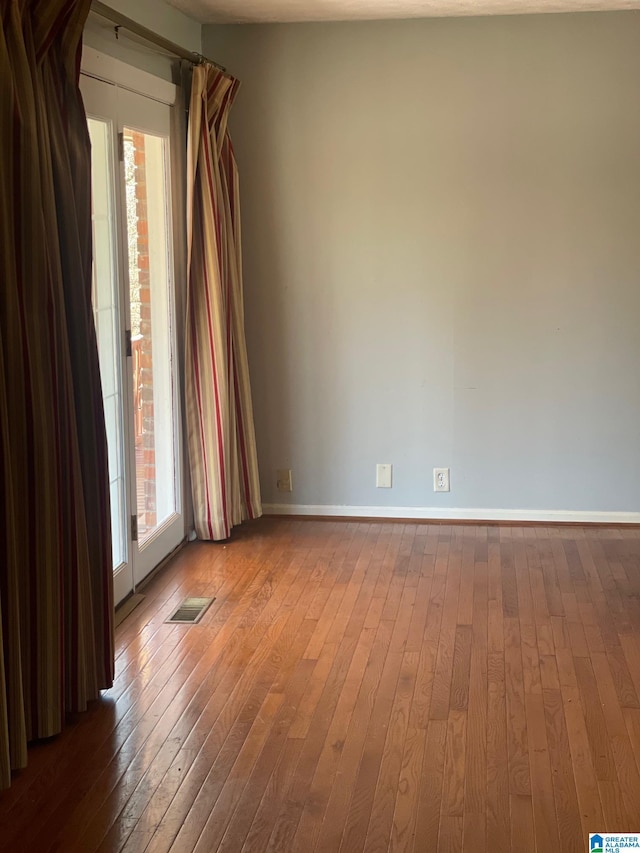 spare room with baseboards, visible vents, a healthy amount of sunlight, and wood-type flooring