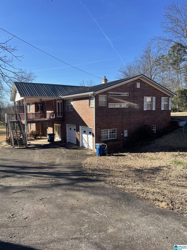 rear view of property with a chimney, aphalt driveway, stairs, brick siding, and an attached garage