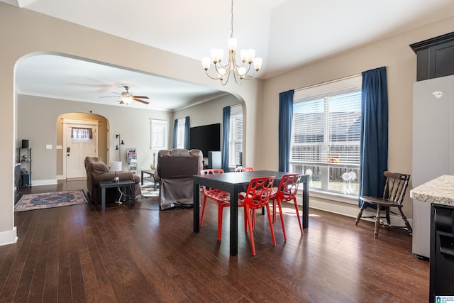 dining room featuring arched walkways, ceiling fan with notable chandelier, baseboards, ornamental molding, and dark wood-style floors