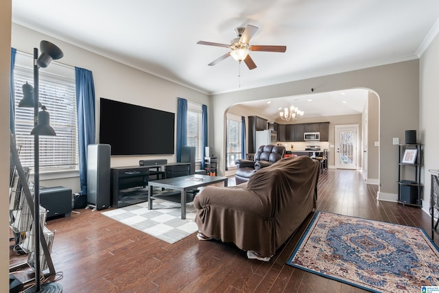 living area with arched walkways, hardwood / wood-style flooring, ceiling fan with notable chandelier, baseboards, and ornamental molding