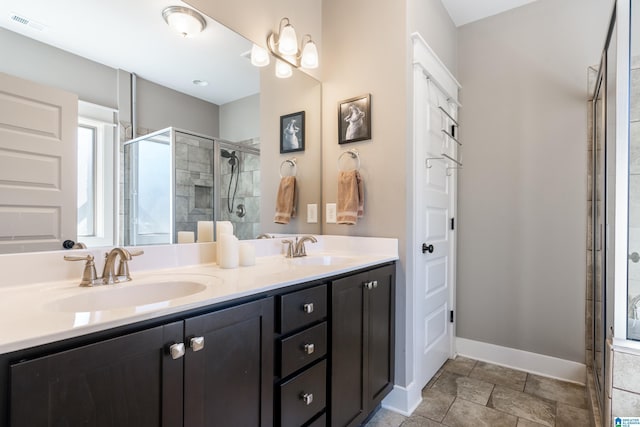 bathroom with a stall shower, a sink, baseboards, and double vanity