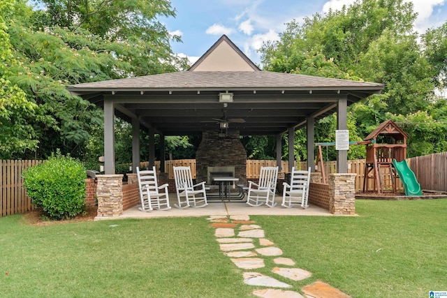 exterior space featuring playground community, an outdoor stone fireplace, a fenced backyard, and ceiling fan