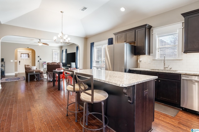 kitchen featuring arched walkways, appliances with stainless steel finishes, open floor plan, vaulted ceiling, and a sink