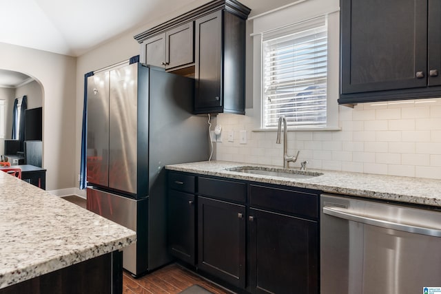 kitchen with stainless steel appliances, dark wood-style flooring, a sink, vaulted ceiling, and backsplash