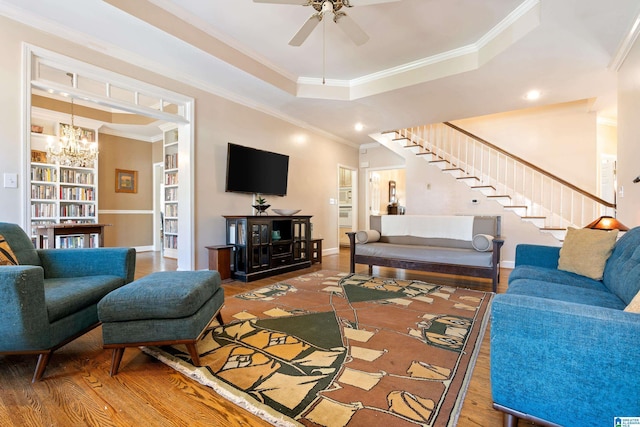 living room with a raised ceiling, stairway, ornamental molding, wood finished floors, and ceiling fan with notable chandelier