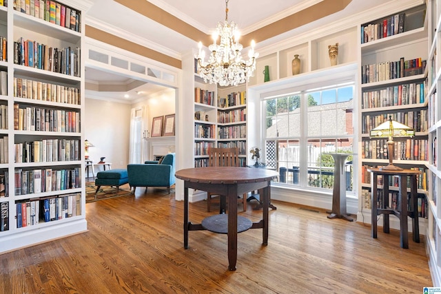 living area featuring crown molding, a notable chandelier, wall of books, and wood finished floors