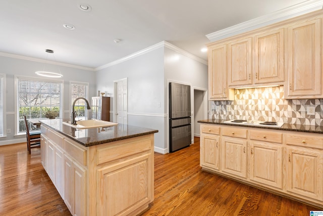 kitchen featuring light brown cabinets, a sink, wood finished floors, tasteful backsplash, and an island with sink