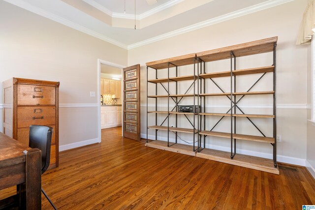 unfurnished office featuring visible vents, baseboards, wood finished floors, a tray ceiling, and crown molding