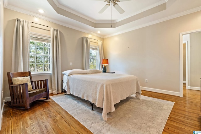 bedroom featuring multiple windows, baseboards, a raised ceiling, and wood finished floors