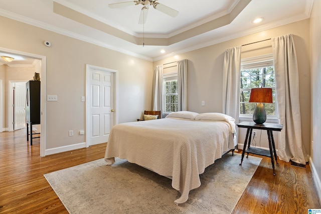 bedroom featuring a raised ceiling, crown molding, baseboards, and wood finished floors