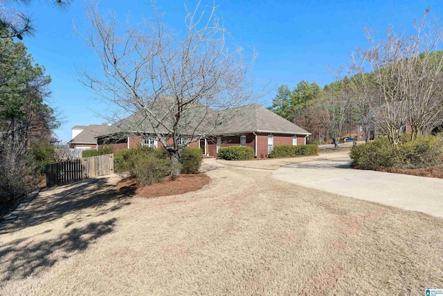 ranch-style house featuring dirt driveway, brick siding, and fence