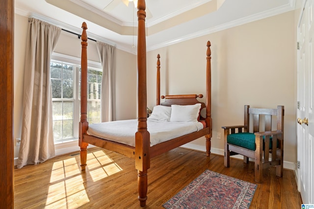 bedroom with ornamental molding, a tray ceiling, baseboards, and wood finished floors