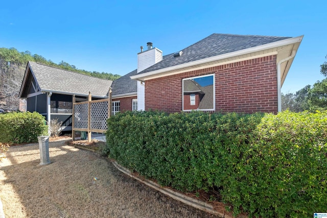 view of property exterior with a shingled roof, a chimney, and brick siding