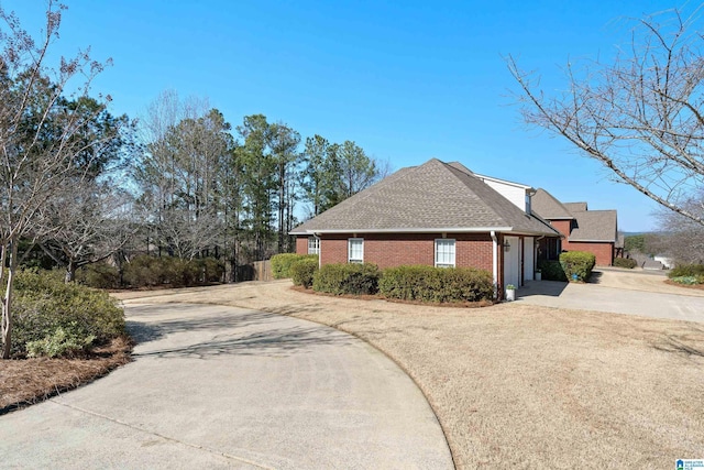 view of side of home featuring a garage, a shingled roof, concrete driveway, and brick siding