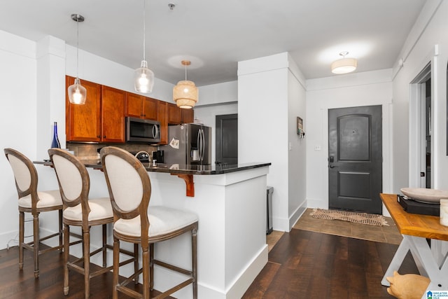 kitchen featuring stainless steel appliances, dark wood-style flooring, a peninsula, and backsplash