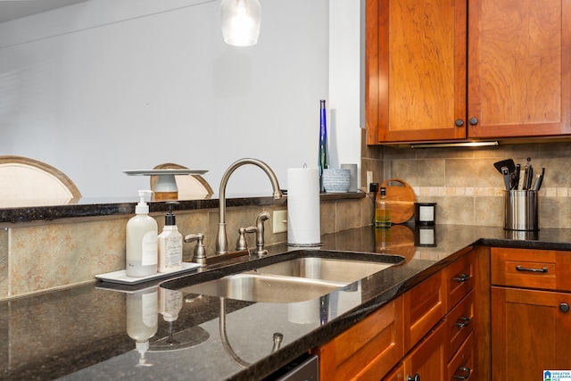 kitchen with brown cabinetry, dark stone countertops, decorative backsplash, and a sink