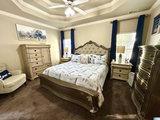 bedroom with a tray ceiling, crown molding, visible vents, dark carpet, and a ceiling fan