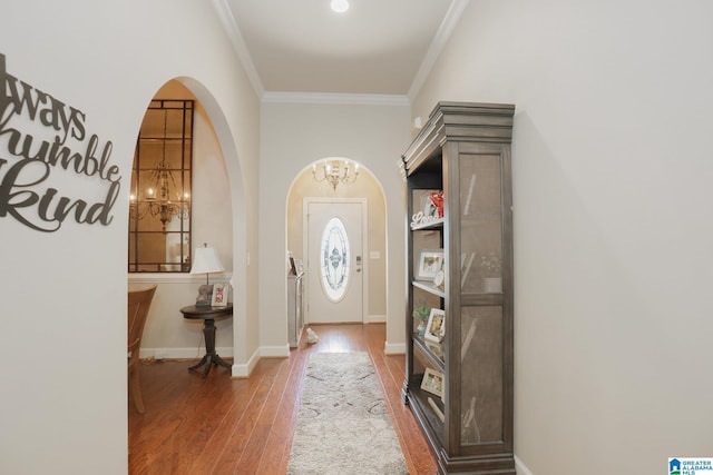 foyer entrance featuring baseboards, crown molding, arched walkways, and wood finished floors