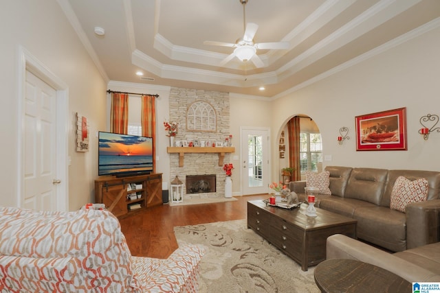 living room featuring arched walkways, a tray ceiling, a fireplace, ornamental molding, and wood finished floors