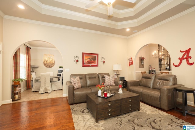 living room with arched walkways, a tray ceiling, crown molding, wood finished floors, and ceiling fan with notable chandelier