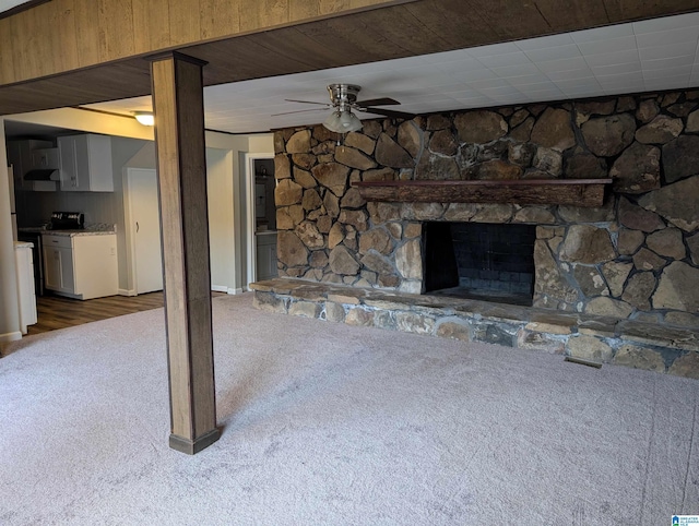unfurnished living room with dark carpet, ceiling fan, and a stone fireplace