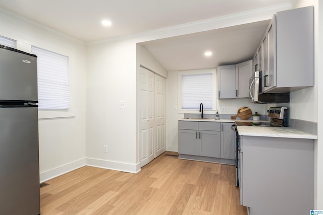 kitchen with gray cabinetry, appliances with stainless steel finishes, a sink, light wood-type flooring, and baseboards