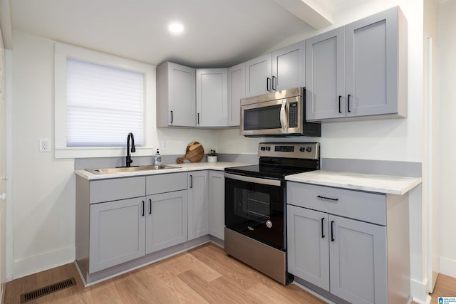 kitchen featuring gray cabinets, stainless steel appliances, light countertops, light wood-style floors, and a sink