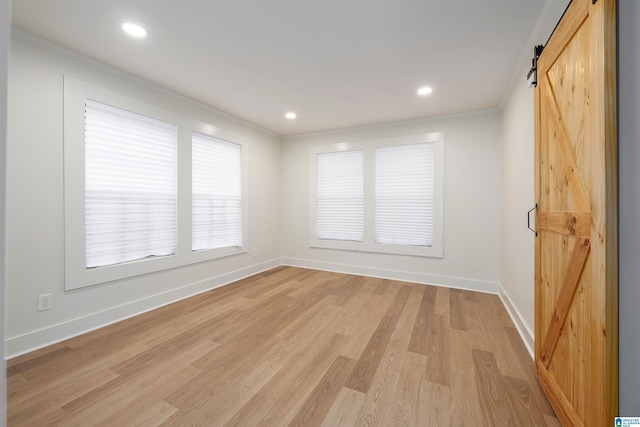 unfurnished room with baseboards, crown molding, light wood finished floors, and a barn door