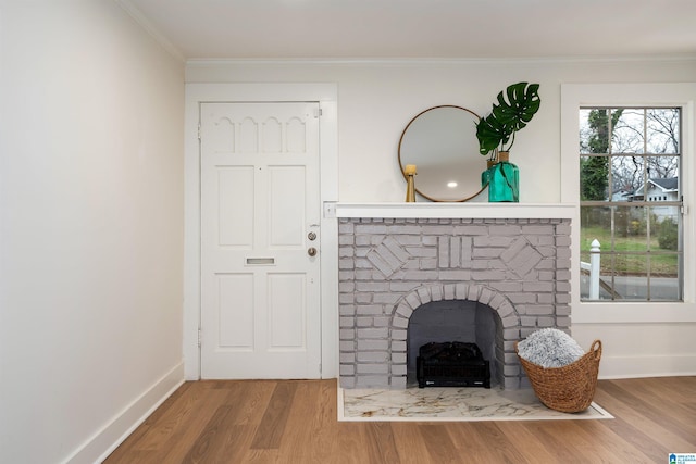 unfurnished living room featuring crown molding, a brick fireplace, wood finished floors, and baseboards