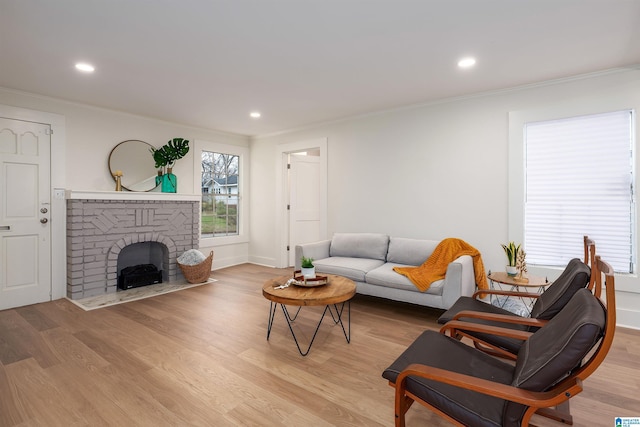 living room with light wood-type flooring, a brick fireplace, and crown molding