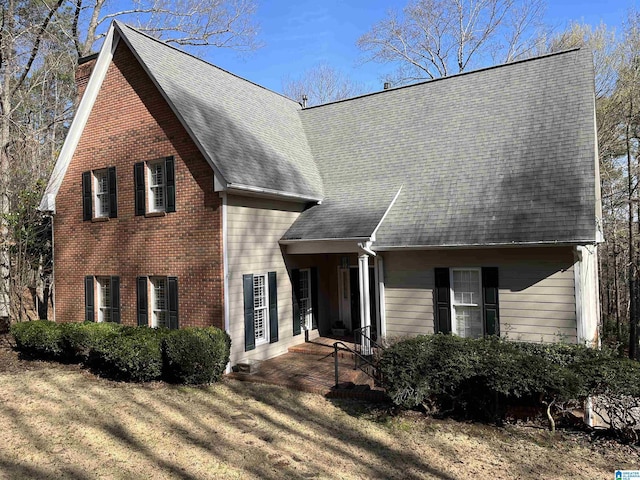 view of front of property with a shingled roof, a front yard, and brick siding