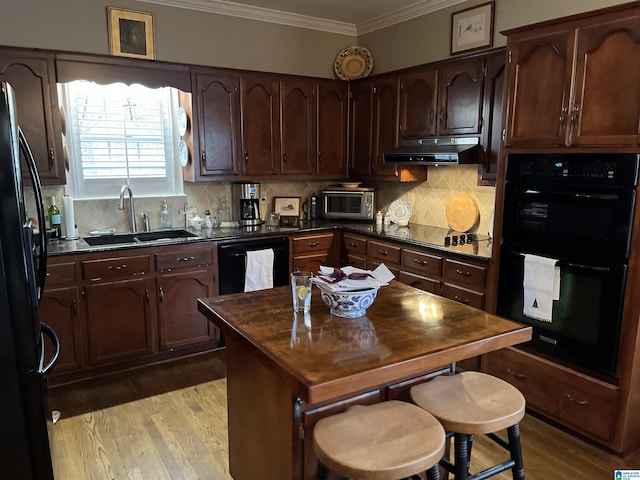 kitchen featuring dark countertops, ornamental molding, under cabinet range hood, black appliances, and a sink