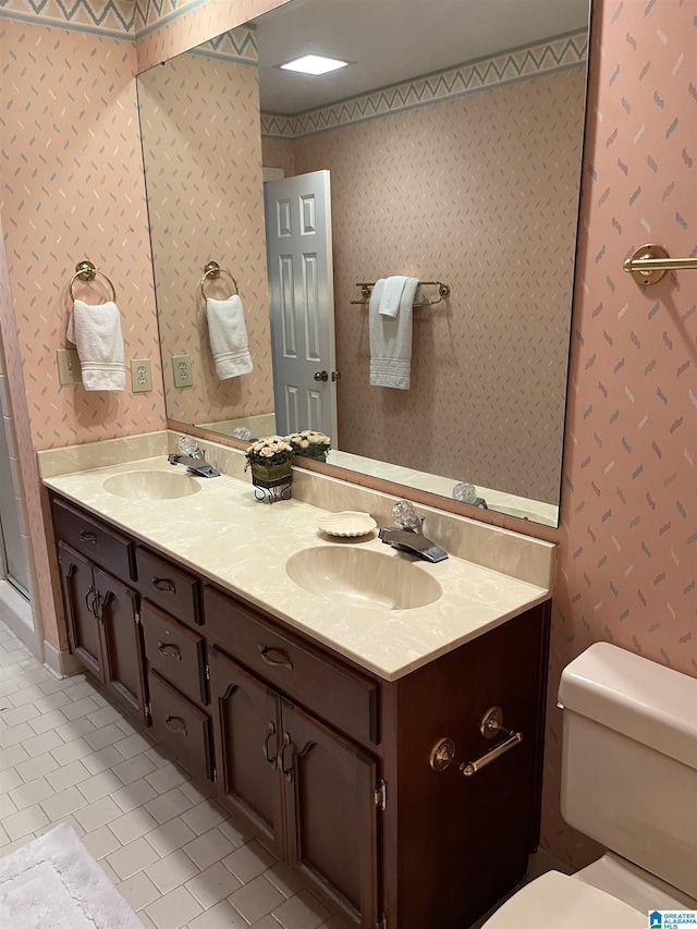 bathroom featuring double vanity, a sink, toilet, and wallpapered walls