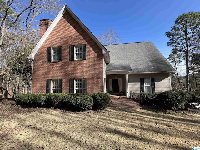 view of front of home with brick siding, a chimney, and a front lawn