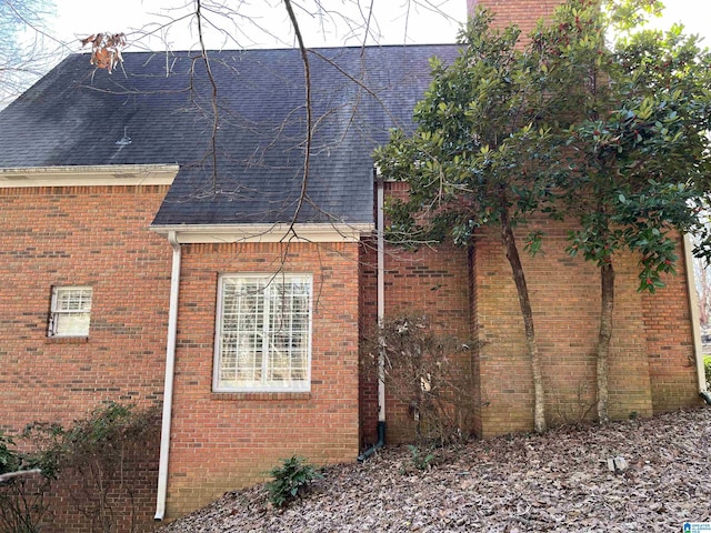 view of side of property featuring brick siding and roof with shingles