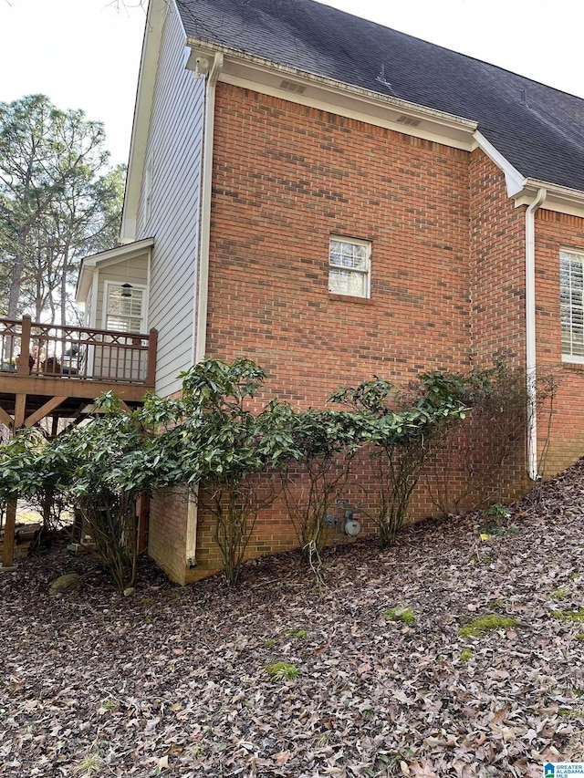 view of side of home featuring a wooden deck, a shingled roof, and brick siding