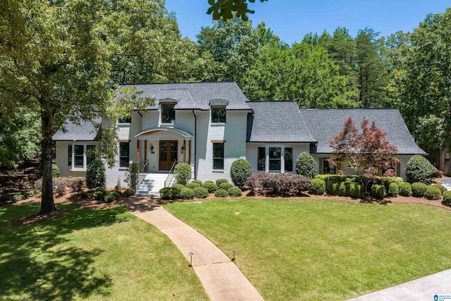 french provincial home featuring a front lawn, roof with shingles, brick siding, and mansard roof