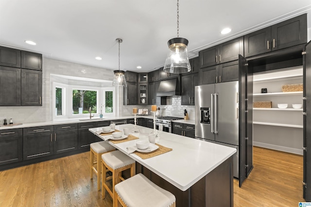 kitchen with high end appliances, light countertops, glass insert cabinets, a kitchen island, and a kitchen breakfast bar