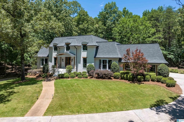 french provincial home with a shingled roof, mansard roof, and a front yard