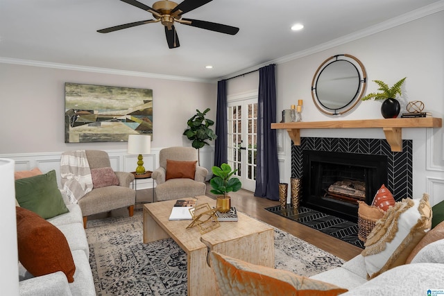 living room featuring crown molding, recessed lighting, wainscoting, wood finished floors, and a tile fireplace