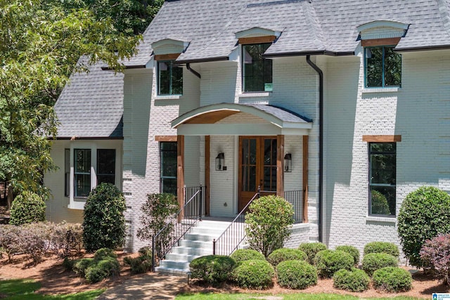 view of front of property featuring stairs, brick siding, and a shingled roof